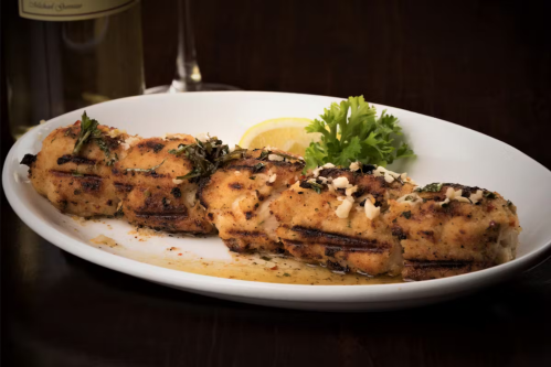 A plate of grilled fish fillets topped with herbs and nuts, garnished with a lemon slice and parsley.
