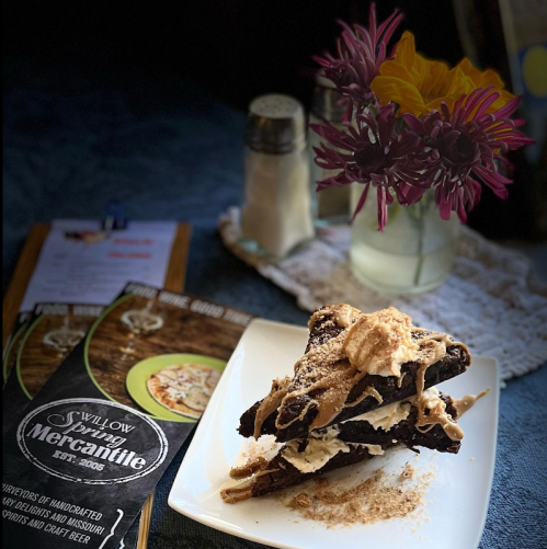 A plate of layered dessert topped with cream and crumbs, with a menu and flowers in the background.