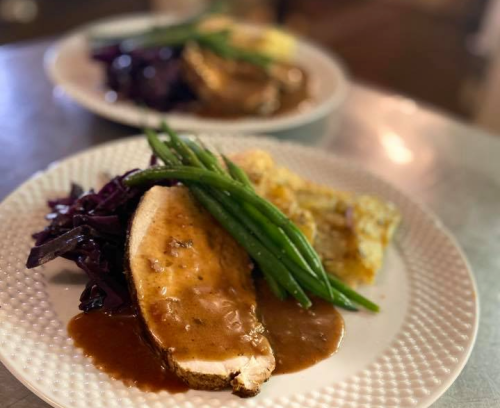 Two plates of food featuring sliced turkey with gravy, green beans, purple cabbage, and a side of casserole.