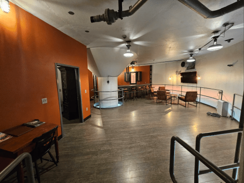 A spacious, modern room with orange walls, wooden flooring, seating areas, and a bar setup.