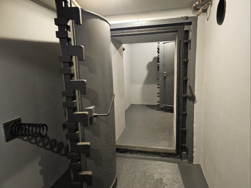 A dimly lit, empty room with two cylindrical structures and a doorway leading to another space.