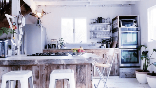 Bright, modern kitchen with wooden accents, a gas stove, and plants, featuring a large island and stainless steel appliances.