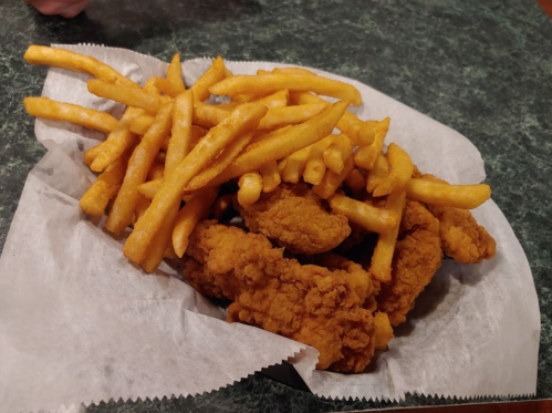 A basket of golden fried chicken tenders served with crispy French fries on a green countertop.