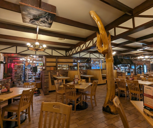 Interior of a rustic restaurant featuring wooden tables, a large tree trunk, and a cozy atmosphere.