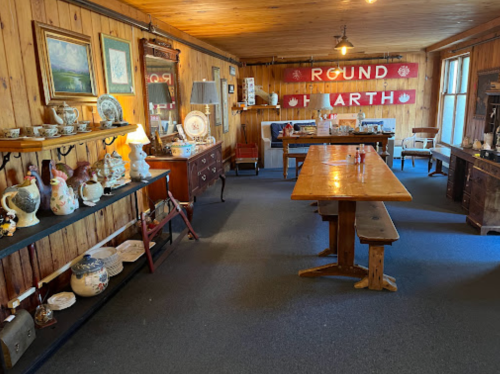 A cozy wooden room filled with antique furniture and decorative items, featuring a long table and various collectibles.