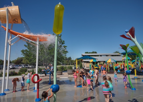 Children playing in a splash pad with colorful water features on a sunny day.