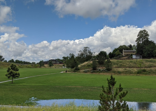 A scenic view of a green park with trees, a path, and fluffy clouds in a blue sky.