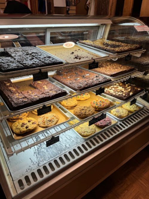 A display case filled with various baked goods, including brownies and cookies, in a cozy bakery setting.