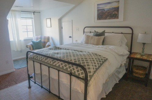Cozy bedroom with a metal bed, soft bedding, a chair, and a window, featuring warm, inviting decor.
