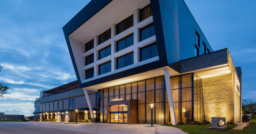 Modern hotel exterior at dusk, featuring a unique architectural design with illuminated entrance and landscaping.