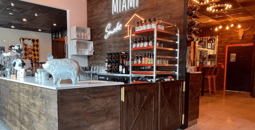 A cozy restaurant interior featuring a wooden bar, shelves of drinks, and a decorative pig statue.