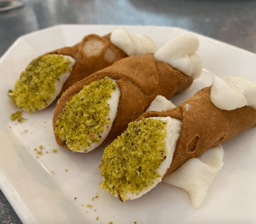 Three cannoli filled with creamy white filling and topped with crushed pistachios on a white plate.