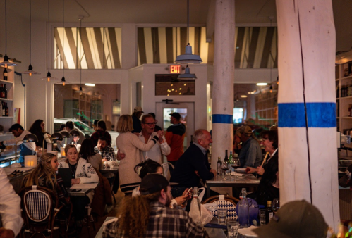 A lively restaurant scene with diners at tables, chatting and enjoying their meals in a warmly lit space.