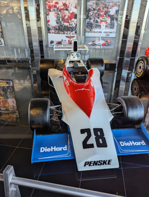 A vintage race car with a red and white design, number 28, displayed in a museum setting.