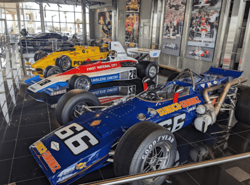Three vintage race cars displayed in a modern showroom, featuring vibrant colors and sleek designs.