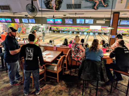A lively bowling alley scene with people eating and socializing, lanes visible in the background.