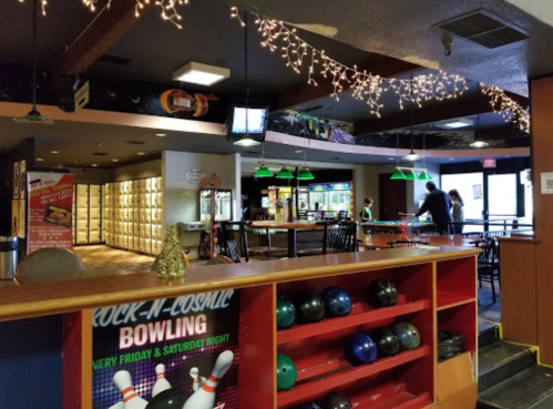 Interior of a bowling alley with festive lights, a bar area, and bowling balls on display. People are enjoying the space.