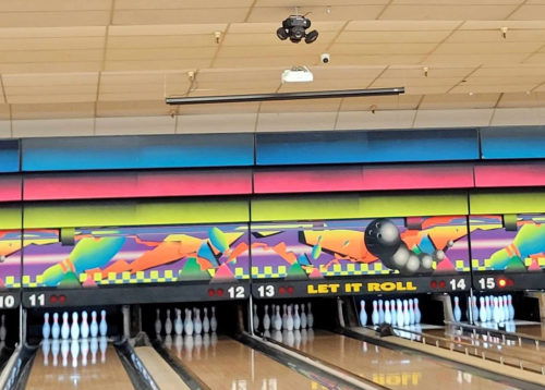 A colorful bowling alley with a mural, bowling pins, and a ball on the lane. The phrase "LET IT ROLL" is visible.