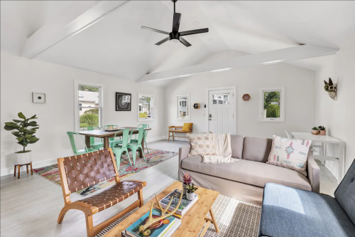 Bright, modern living room with a sofa, coffee table, and dining area featuring a colorful rug and plants.