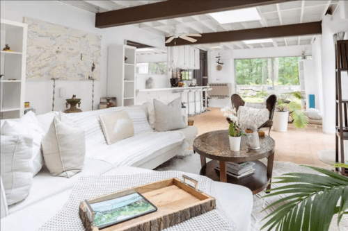 Bright, airy living room with a white sofa, wooden coffee table, and large windows overlooking greenery.