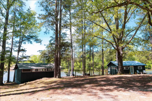 A serene lakeside scene featuring two cabins surrounded by tall trees and a clear blue sky.