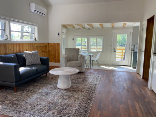 Cozy living room with a dark sofa, round table, and large windows, featuring wooden accents and a view of the outdoors.
