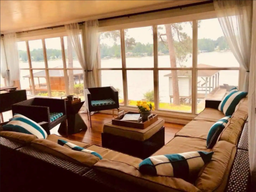 Cozy living room with a sectional sofa, coffee table, and large windows overlooking a lake and trees.