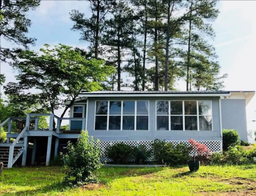 A charming gray house with large windows, surrounded by trees and greenery, featuring a staircase and a small garden.