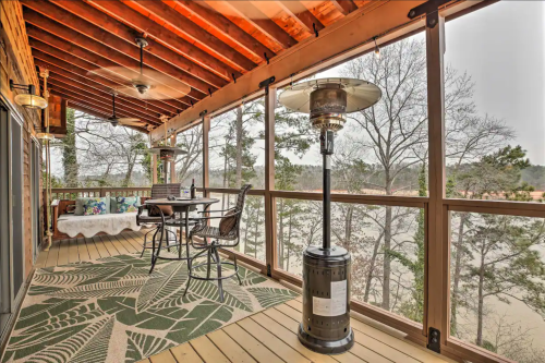 A cozy porch with a dining table, chairs, and a patio heater, surrounded by trees and a scenic view.