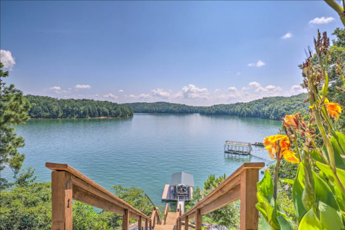 A serene lake view from wooden steps, surrounded by lush greenery and colorful flowers under a clear blue sky.