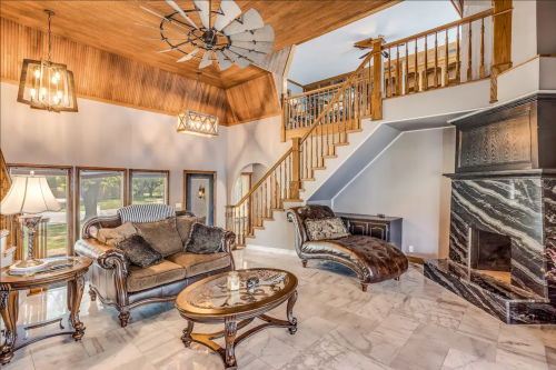 Elegant living room with a staircase, marble flooring, plush furniture, and a stylish fireplace. Bright and inviting atmosphere.