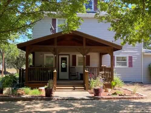 A charming two-story house with a wooden porch, surrounded by trees and a landscaped yard.