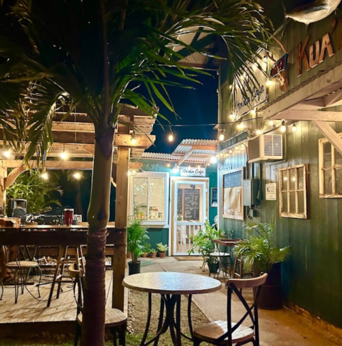 Cozy outdoor café at night, featuring string lights, wooden tables, and lush greenery.