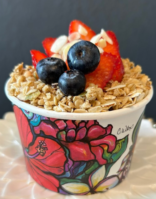 A colorful cup filled with granola, topped with strawberries, blueberries, and sliced almonds against a dark background.