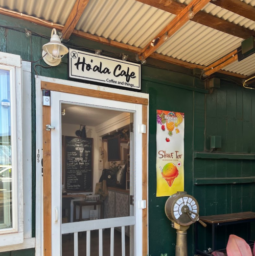 Exterior of Hiola Cafe with a sign, menu board, and a colorful poster on a green wall.