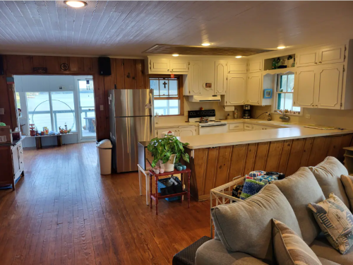 Cozy kitchen and living area with wooden walls, a large island, and natural light from windows.