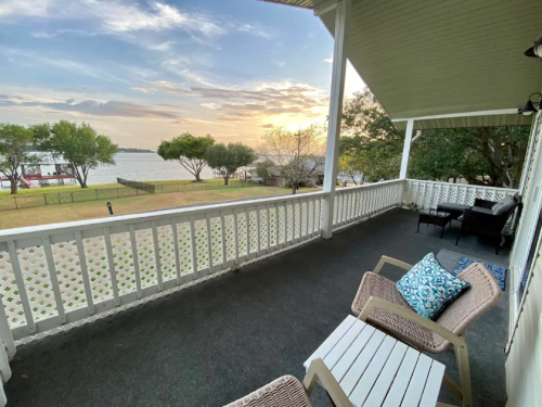 A serene porch view overlooking a lake at sunset, featuring white chairs and a cozy atmosphere.