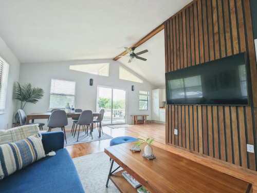 Bright, modern living room with wooden accents, a large TV, and a dining area featuring a table and chairs.
