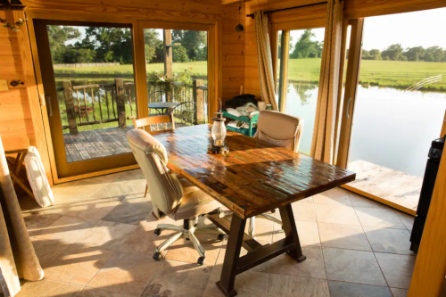 A cozy wooden dining area with a large table and chairs, overlooking a serene outdoor view by a pond.