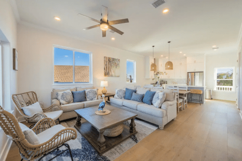 Bright, modern living room with a light sofa, decorative pillows, a wooden coffee table, and open kitchen in the background.