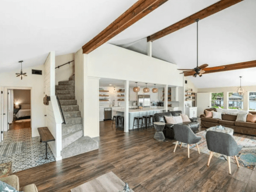 Bright, modern living space with wooden beams, a staircase, and an open kitchen, featuring cozy seating and stylish decor.