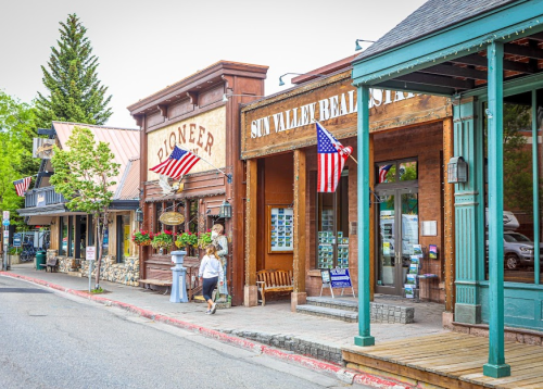 A charming street scene featuring rustic storefronts with American flags and a pedestrian walking by.