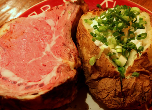 A plate featuring a juicy prime rib steak alongside a baked potato topped with green onions and sour cream.