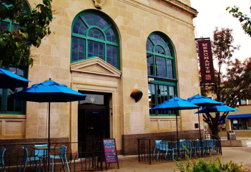 Exterior of a restaurant with blue umbrellas, a sign reading "Merchants," and large arched windows.