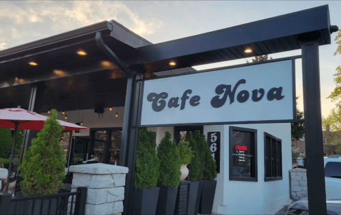 Exterior of Cafe Nova featuring a sign, outdoor seating, and decorative plants.