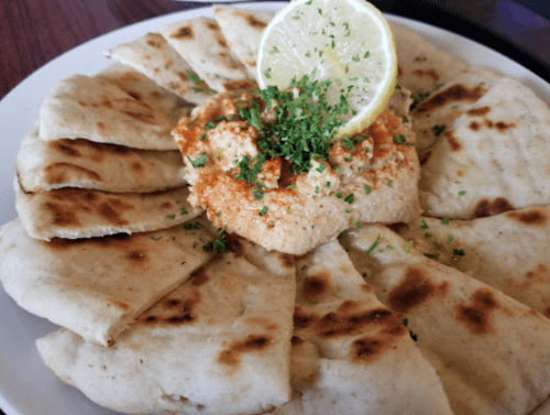 A plate of flatbread arranged around a bowl of hummus, garnished with lemon and herbs.