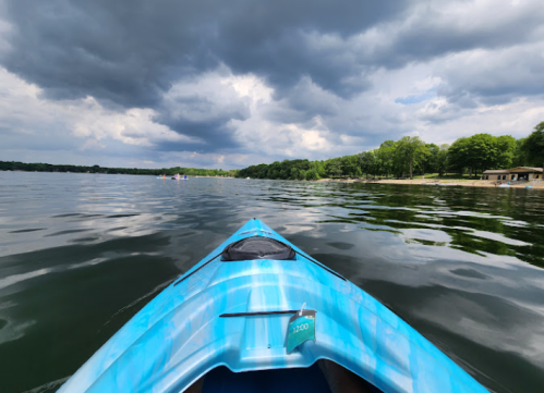 A blue kayak on calm water, with dark clouds overhead and a shoreline of trees in the distance.
