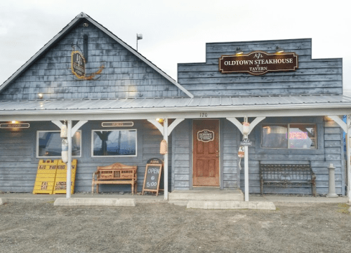 Exterior of Oldtown Steakhouse Tavern, featuring a wooden facade, open sign, and benches outside.