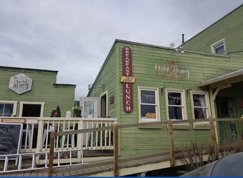 A green wooden building with signs for "Breakfast and Lunch" and "Wild Honey," featuring a porch and cloudy sky.