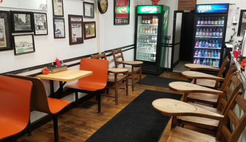 A cozy diner interior with orange chairs, wooden tables, and vending machines in the background.